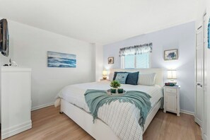 A bedroom with a bed, bedside tables, a television, and artwork on the walls. - Crescent Towers II 508-Oceanfront Corner Unit-2BR (North Myrtle Beach)