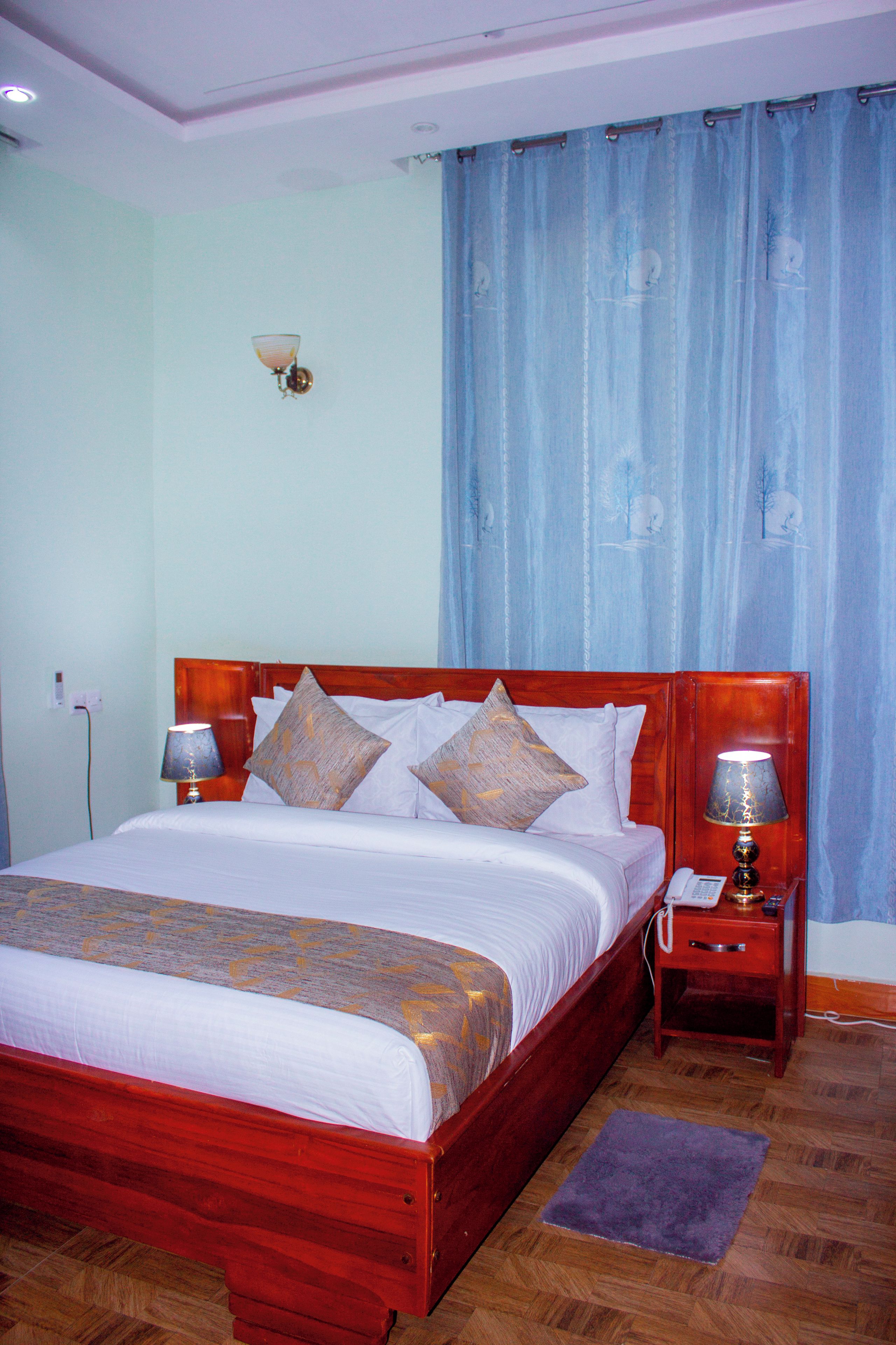Una habitación de hotel con una cama de madera, dos lámparas de noche, un teléfono y una cortina azul.
