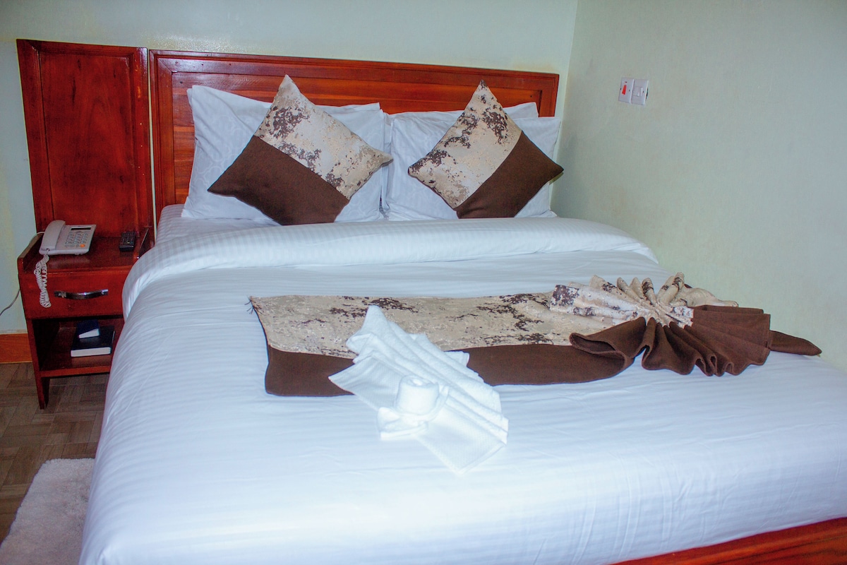 Cama de casal com cabeceira de madeira, duas almofadas, lençol branco e manta marrom.