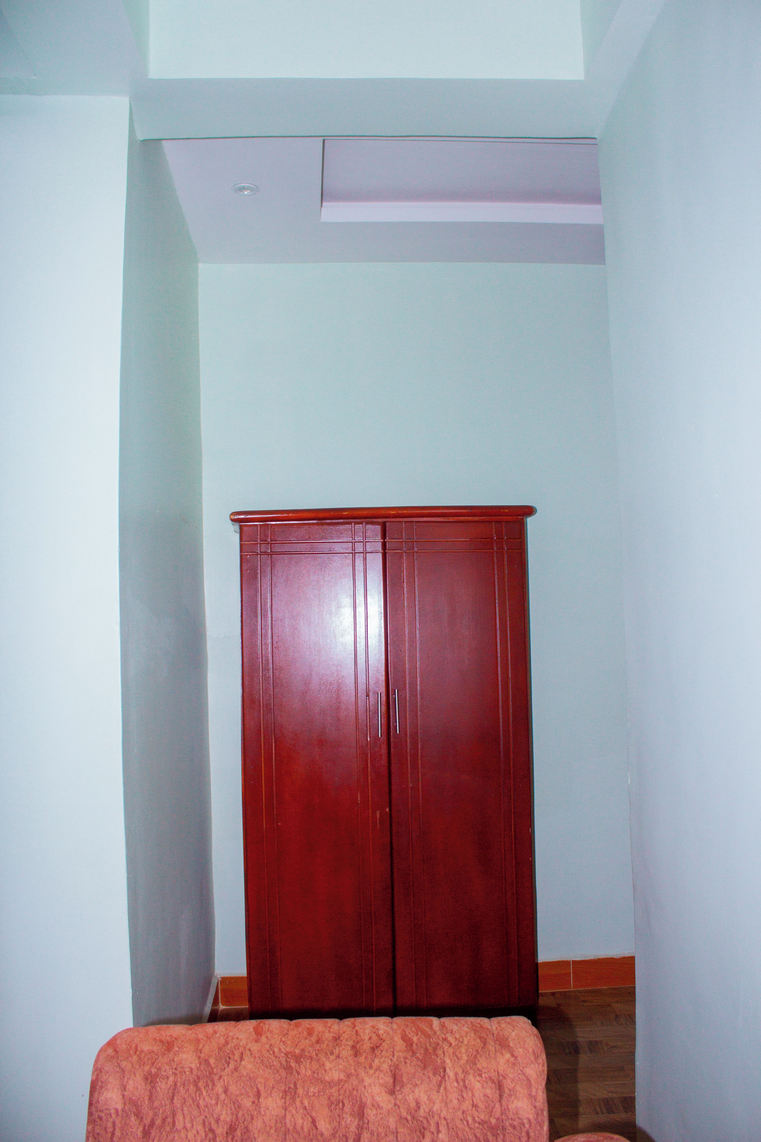 A room with a wooden wardrobe, a patterned sofa, and a light-colored wall.