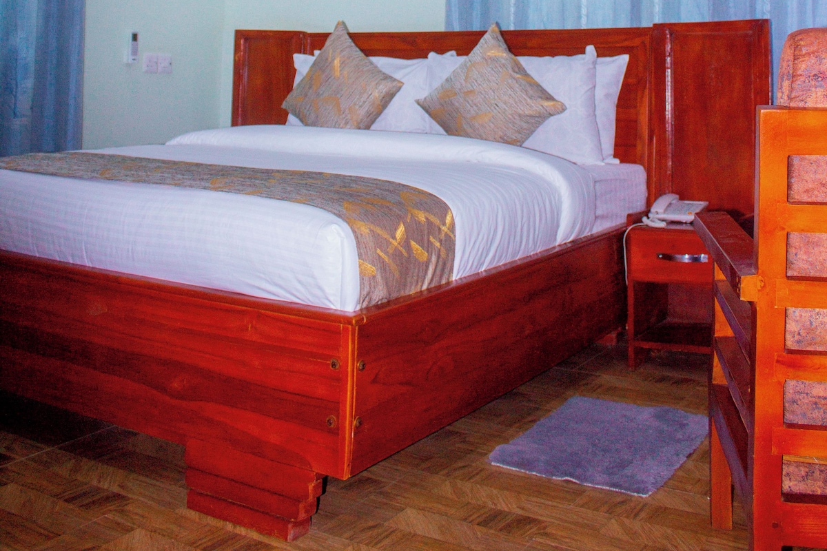 Quarto de hotel com cama de madeira, mesa de cabeceira, telefone e escrivaninha com cadeira.