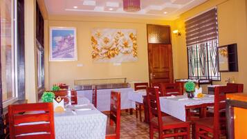 Ein Restaurantinneres mit Holztischen, Stühlen und einer Wand mit Gemälde und floralem Dekor.