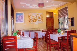 Interior de restaurante com mesas e cadeiras de madeira, e uma parede decorativa com pintura e motivos florais.