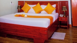 A hotel room with a large bed, a painting of a sunset, and a wooden floor. - Kibui Hotel Ilazo (Dodoma)