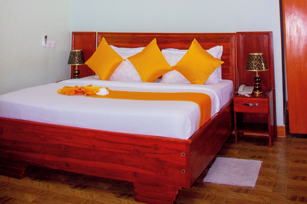 Quarto de hotel com uma cama grande, um quadro de um pôr do sol e piso de madeira.