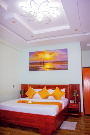 Quarto de hotel com uma cama grande, um quadro de um pôr do sol e piso de madeira.