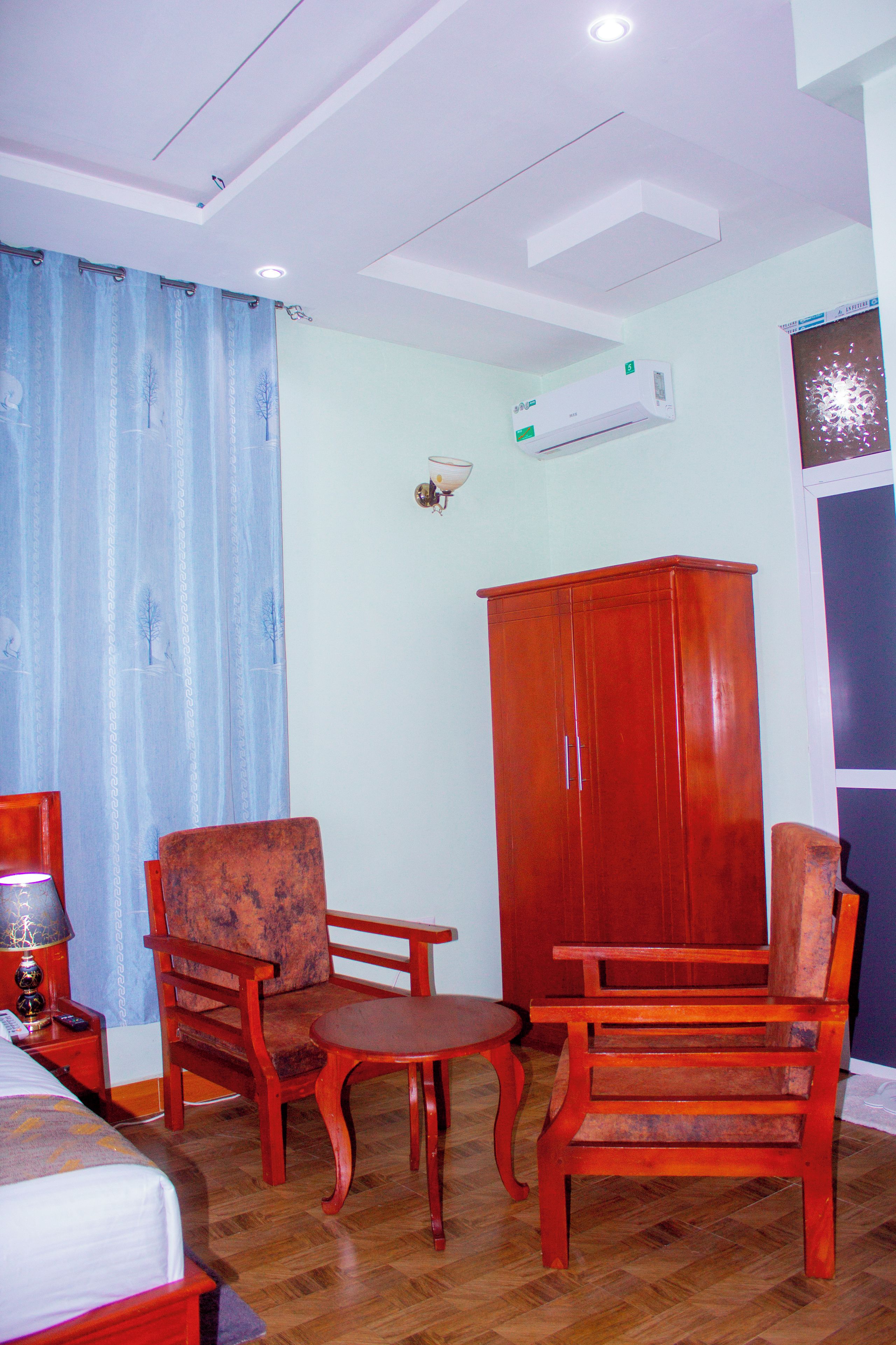 A hotel room with a bed, a wooden wardrobe, two armchairs, a small table, and a wall-mounted air conditioner.