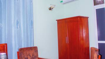 A hotel room with a bed, a wooden wardrobe, two armchairs, a small table, and a wall-mounted air conditioner.