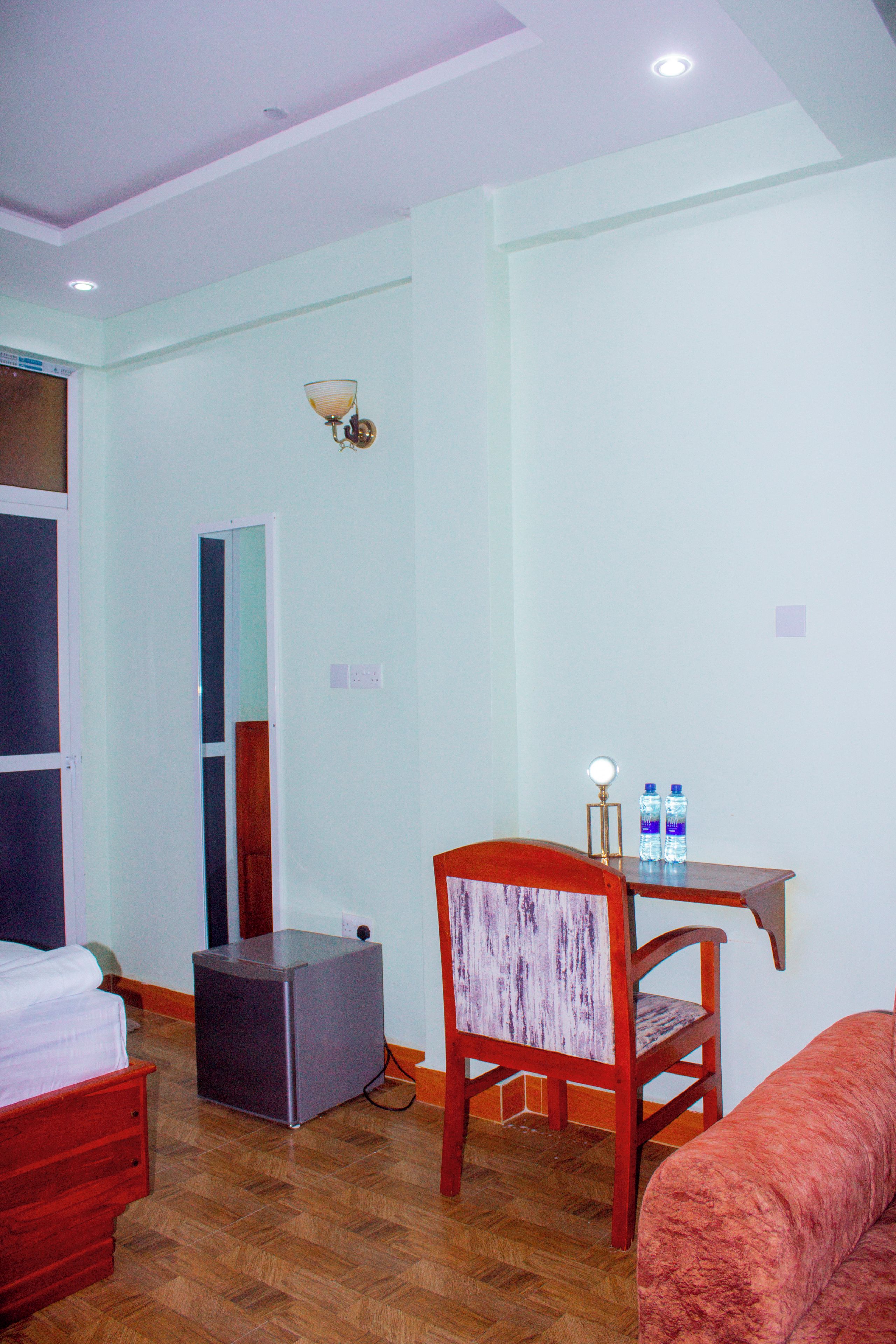 A hotel room with a bed, a desk with a chair, a small table with water bottles, and a heater.