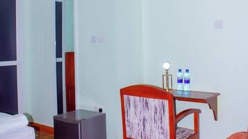 A hotel room with a bed, a desk with a chair, a small table with water bottles, and a heater.