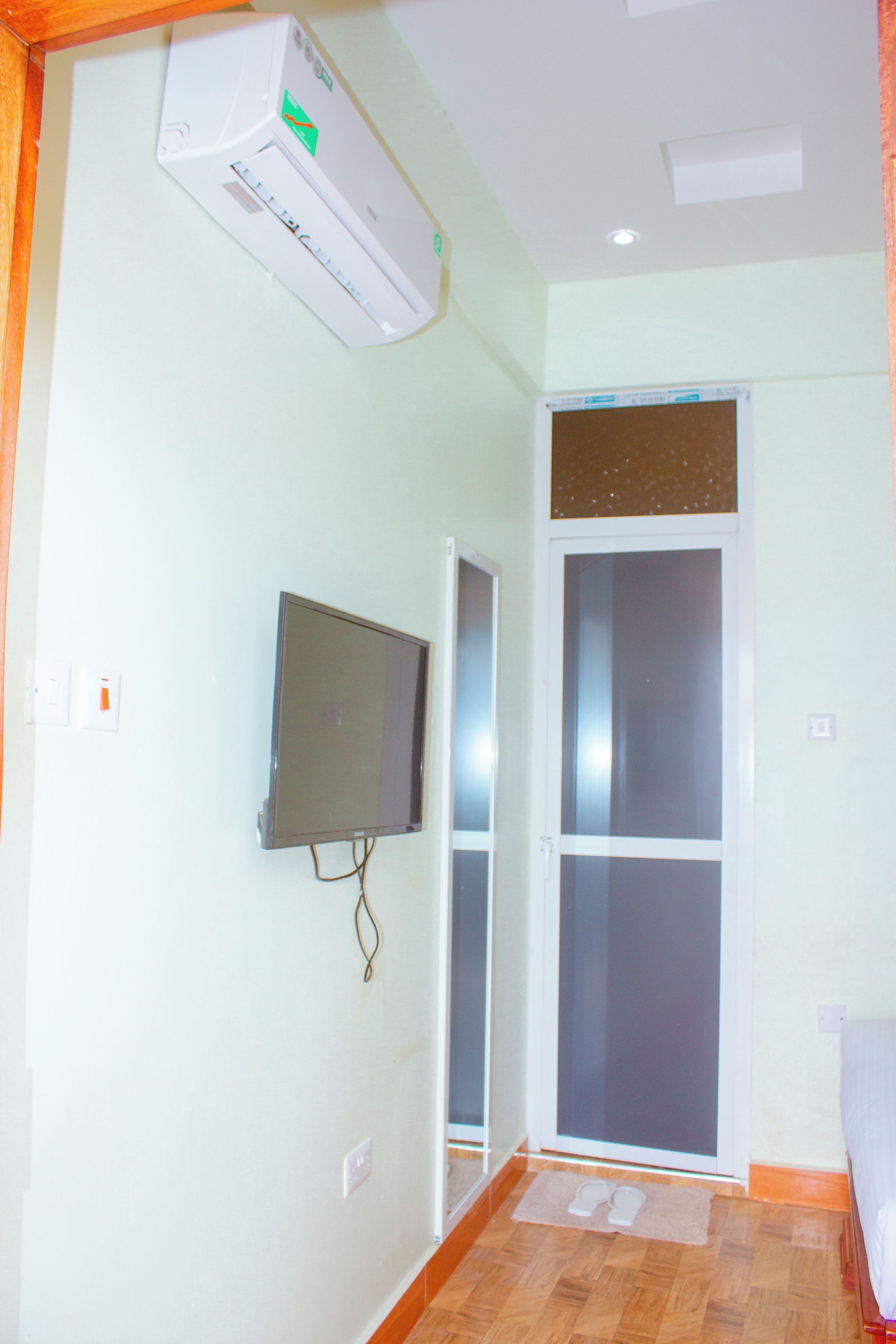 A room with a mounted air conditioner, a television on the wall, and a sliding glass door.