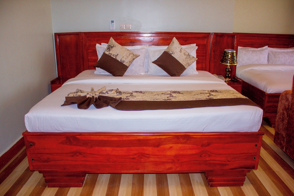 Uma cama grande com estrutura de madeira, roupa de cama branca e duas almofadas decorativas.