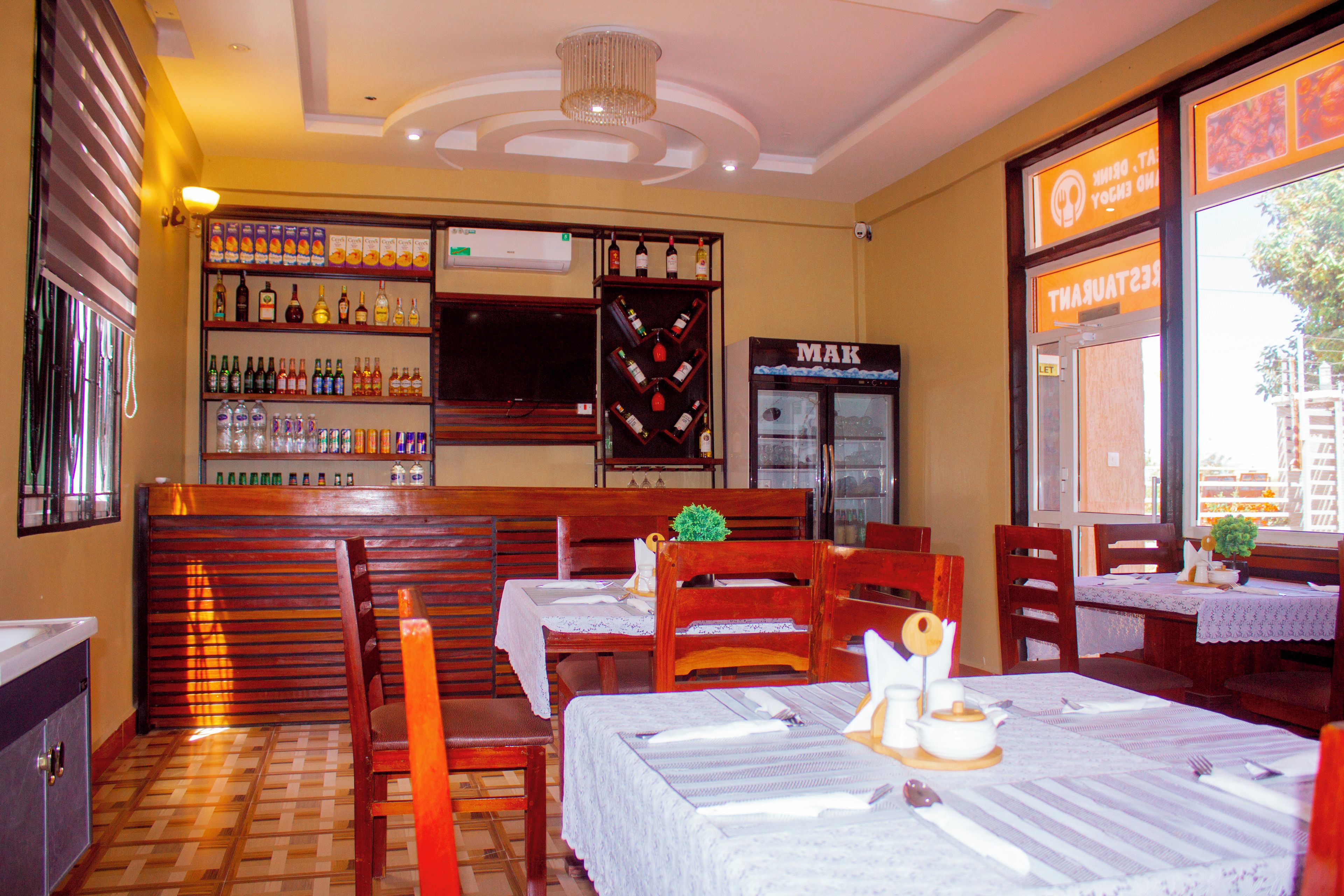 Interior de un restaurante con muebles de madera, una zona de bar con botellas y un refrigerador con la etiqueta 'MAK'.