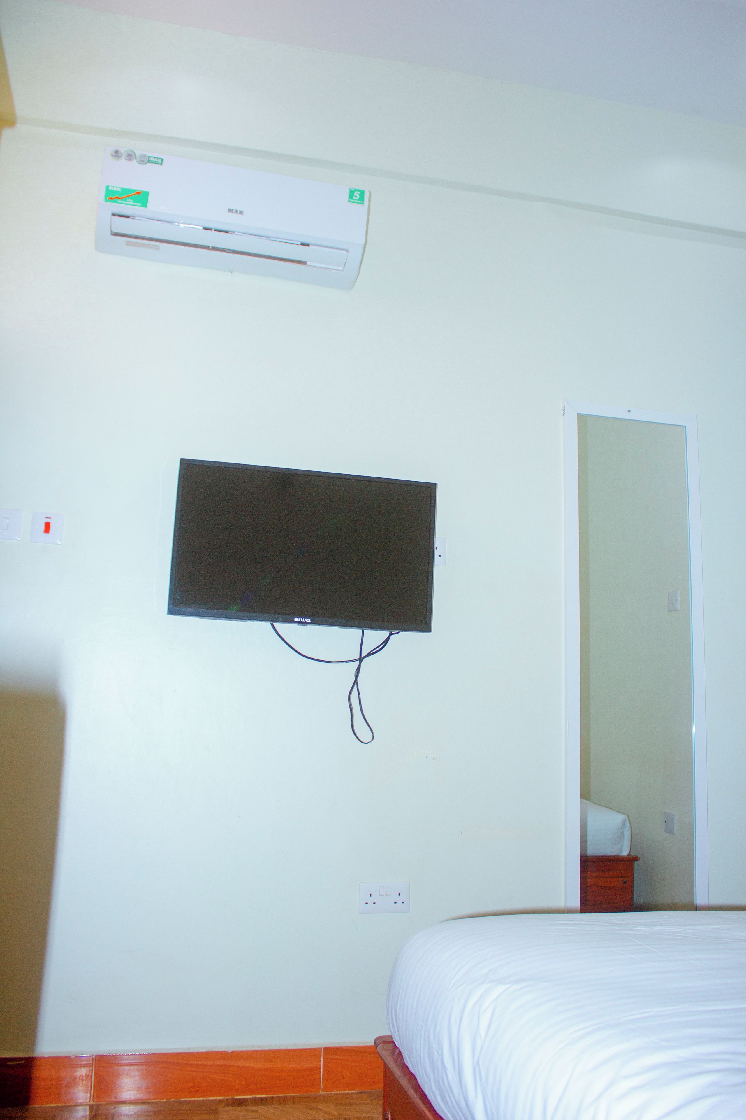 Ein Zimmer mit einem Bett, einem wandmontierten Flachbildfernseher und einer Klimaanlage darüber.