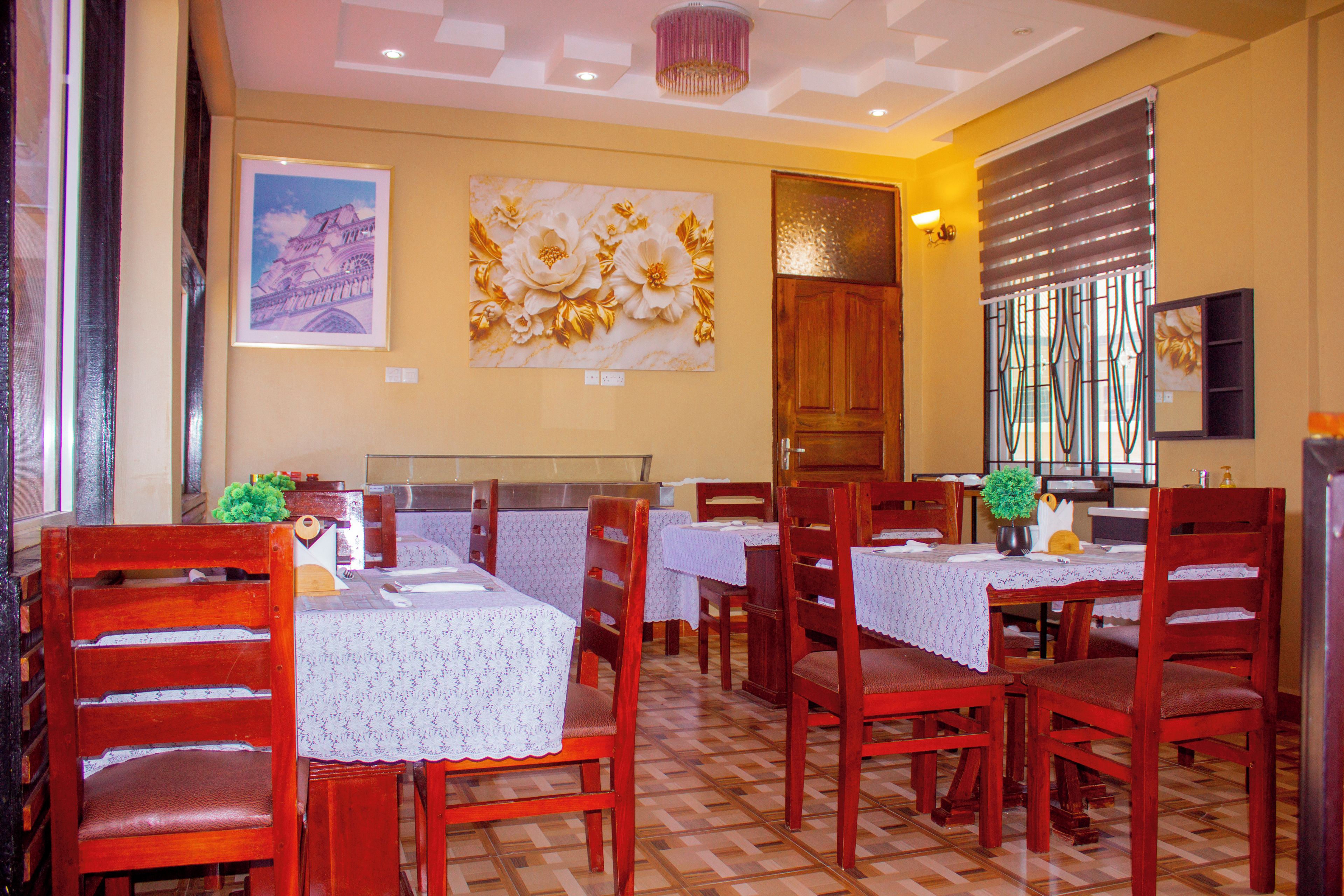 Un comedor con sillas y mesas de madera, una araña y obras de arte en las paredes.