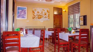 Un comedor con sillas y mesas de madera, una araña y obras de arte en las paredes.