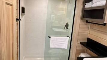 Casa de banho compacta com cabine de chuveiro em vidro, sanita branca e lavatório embutido com bancada.