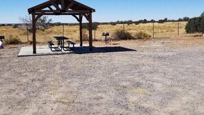 Un espace de pique-nique abrité, doté de bancs et d’une table, entouré d’un paysage aride et dégagé.