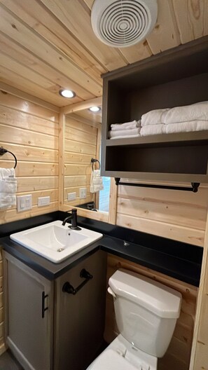 Ein kleines Badezimmer mit Holzwänden, einem Waschbecken, einer Toilette und einem Regal mit gefalteten Handtüchern.