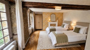 Un dormitorio con dos camas, techo de madera, pared de piedra, una ventana y un espejo.
