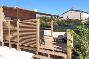 A wooden deck with a covered seating area, a pool, and a building in the background. - Hyeres Stay Near the Beach (Hyères)