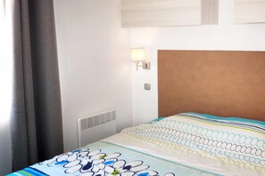A hotel room with a bed, a wall-mounted lamp, and a window with curtains. - Hyeres Stay Near the Beach (Hyères)