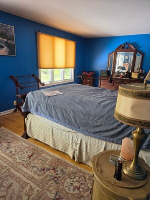 Ein Schlafzimmer mit einem großen Bett, einem Schminktisch, einem Spiegel und einem Fenster mit Jalousien.