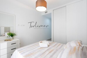 Ein Schlafzimmer mit einem Bett, einem Nachttisch mit Pflanze, einer Wandleuchte und einer Wand mit einem Schild.