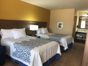 Habitación de hotel con dos camas, una mesita de noche, una lámpara, un espejo y zona de baño.