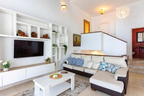 A modern living room with a flat-screen TV, white shelving, a sofa with patterned cushions, and a staircase leading to a red-tiled bathroom. - Todimer Luxury Villa Herradura (Almuñécar)