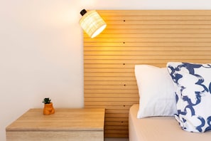 Un dormitorio con cabecera de madera, mesita de noche con una planta pequeña y cama con almohadas estampadas.