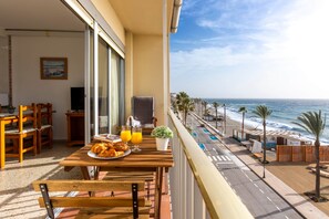 A balcony with a dining table set with croissants and orange juice, overlooking a beach with palm trees and a clear sky. - Todimer Neptuno Beach (Torrenueva Costa)