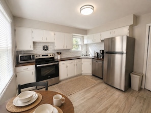 A modern kitchen with white cabinets, stainless steel appliances, and a wooden dining table with a placemat. - Perfect Saratoga Location: beautiful 4-bedroom house near downtown & SPA Park (Saratoga Springs)