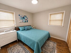 Een slaapkamer met een bed, twee nachtkastjes, een wandlamp, een schilderij en twee tapijten.