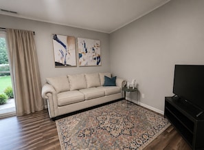 A living room with a beige sofa, a patterned rug, a television, and abstract art on the wall. - Perfect Saratoga Location: beautiful 4-bedroom house near downtown & SPA Park (Saratoga Springs)