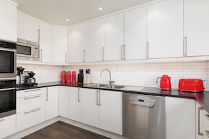 A modern kitchen with white cabinetry, stainless steel appliances, and a black countertop. - Unique property with its own beachfront for rent - Kystperlen Lysøysundet (Trøndelag)