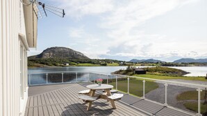 Une terrasse en bois avec une table et des chaises, offrant une vue sur un lac et des montagnes.