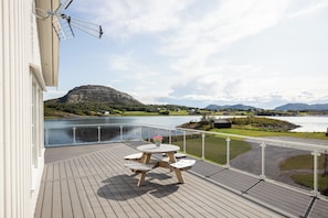 Une terrasse en bois avec une table et des chaises, offrant une vue sur un lac et des montagnes.