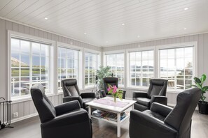 A sunroom with large windows, black leather chairs, a white coffee table, and a potted plant.