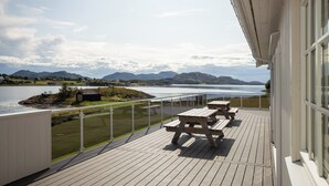 Une terrasse avec des tables de pique-nique offrant une vue sur un lac et des montagnes.