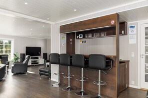 A modern bar area with four stools, a television, and a wooden shelf with glasses. - Unique property with its own beachfront for rent - Kystperlen Lysøysundet (Trøndelag)