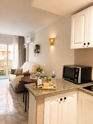 A modern kitchen with a built-in microwave, a dining area with a table and chairs, and a living room with a sofa and a plant. - Apartment in Benalmadena near the beach and the pool. At Bonanza Square (Benalmádena)