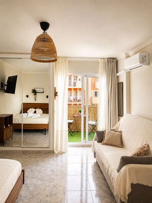 A hotel room with a bed, a sofa, a TV, a mirror, and a balcony with a view of the building. - Apartment in Benalmadena near the beach and the pool. At Bonanza Square (Benalmádena)