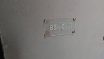 A metal plate with the number 'B5-0-3' affixed to a wall.