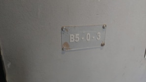 A metal plate with the number 'B5-0-3' affixed to a wall.