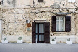 A building with a stone facade, a door with dark shutters, and a window with shutters. - Vacation Home in Salento, in the historic center of Lecce, just a stone's throw from the Duomo! (Lecce)