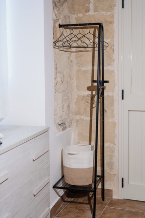 A metal drying rack with clothes hangers and a basket against a textured wall. - Vacation Home in Salento, in the historic center of Lecce, just a stone's throw from the Duomo! (Lecce)
