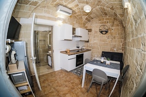 A compact kitchen with a stone wall, a dining area with a table and chairs, and a built-in oven. - Vacation Home in Salento, in the historic center of Lecce, just a stone's throw from the Duomo! (Lecce)