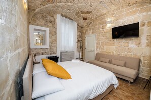 A bedroom with a stone wall, a bed with white and yellow bedding, a sofa, a television, and a mirror. - Vacation Home in Salento, in the historic center of Lecce, just a stone's throw from the Duomo! (Lecce)