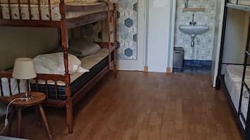 Et værelse med to køjesenge, et lille bord med en lampe, en dør med geometriske mønstre, og et håndvask i det tilstødende rum.